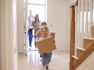 a little girl carrying a cardboard box down a hallway.